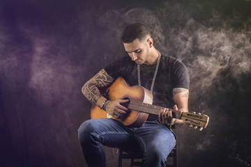 Obraz premium Portrait of hipster playing guitar against black background, in studio shot