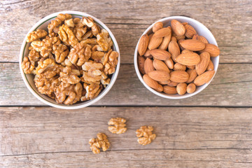 Two ceramic bowls full of walnuts and almonds on the wooden table