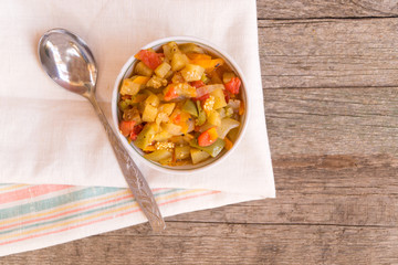 Stew from aubergines, tomatoes, onions, carrots and peppers with metal spoon on the wooden background