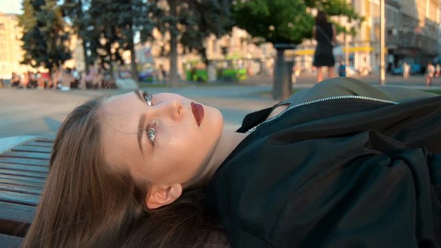the beautiful young lady is lying on a bench on the street