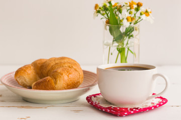 Homemade croissant on plate served with black coffee or americano. Delicious and quick breakfast with fresh croissant and coffee. Croissant and black coffee ready to served for breakfast on wood table