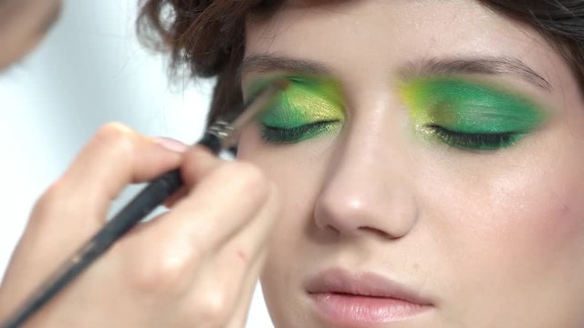 Makeup artist applying eyeshadow. Face of pretty girl, cosmetics. Model beauty tricks.