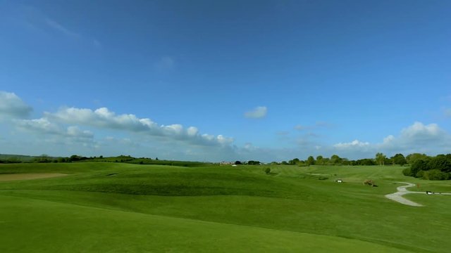 Pan shot of a green golf course on a bright sunny day. Idyllic summer landscape. Sport, relax, recreation and leisure concept.