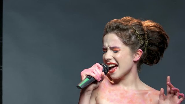 Young woman with microphone singing. Female singer, colorful makeup. How to discover your talent.
