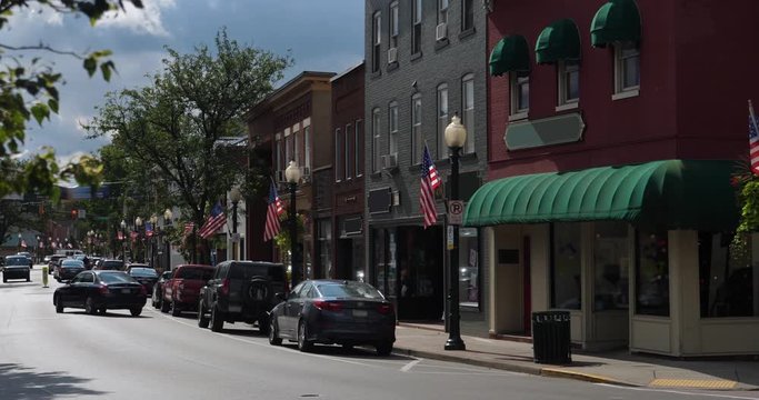 A morning exterior establishing shot of a generic small town's Main Street shopping district storefronts and traffic. Store marquees digitally removed for customization.  	
