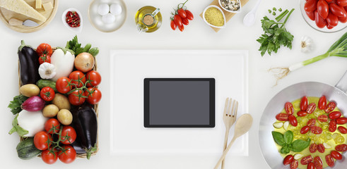 digital tablet above on white cutting board with vegetables, saucepan and ingredients on kitchen white wooden worktop, copy space, top view