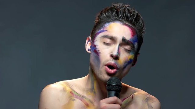 Man with microphone singing. Young male, artistic makeup.