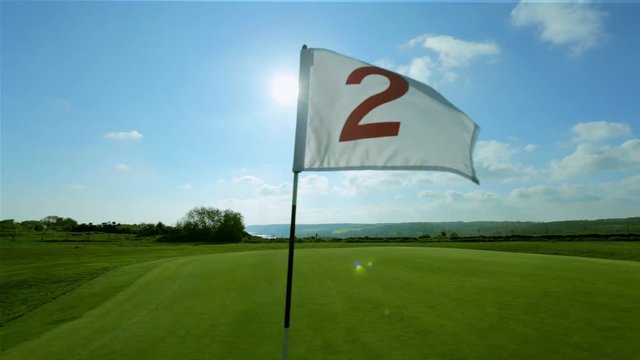 Pan shot of a green golf course, hole and flag on a bright sunny day. Sport, relax, recreation and leisure concept. Summer landscape with sunbeams in the sky