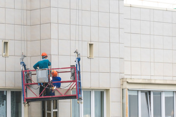 Installers in the construction cradle repair the facade of a house.