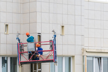 Installers in the construction cradle renovating the facade of a house.