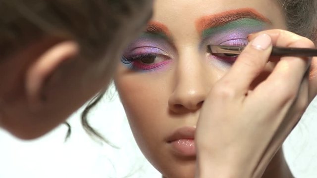 Visagist is applying eyeshadow. Female face, colorful artistic makeup.