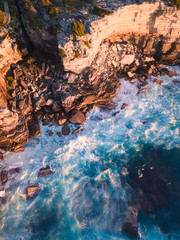 Aerial view of incoming waves into a rock cliff.