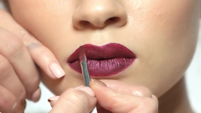 Brush applying dark red lipstick. Plump lips, makeup.