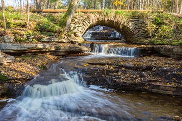 Stream running into a ravine, with an old arch bridge
