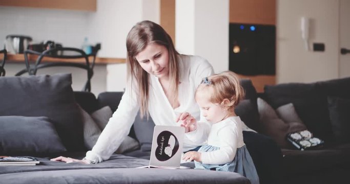 Mother is playing with child at home. Slow Motion 120 fps 4K. Young mom reading a picture book to her baby daughter. Happy motherhood and childhood concept. Toddler girl 1 year old. Cinematic family