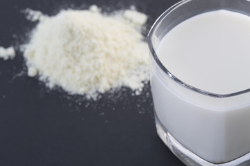 Powdered milk and glass cup of milk on the black background.