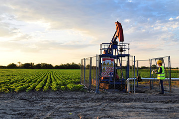 A female engineer at work on an European oil well during dusk time, agriculture field in background...