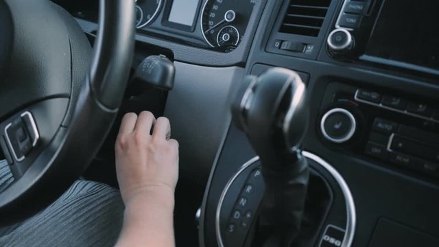 Grey colours shot of female hand starting modern classic car with automatic transmission and gear shift, presses button on key chain to pop out key amd put into ignition