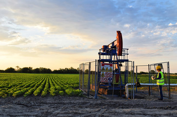 Fototapeta na wymiar A female engineer at work on an European oil well during dusk time, agriculture field in background 