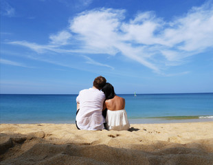 A happy couple in white sitting together looking a beach