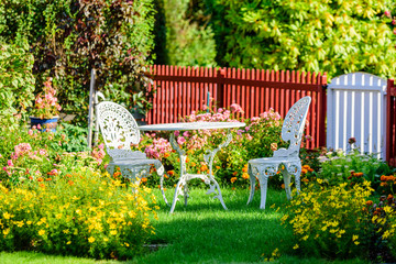 White metal garden furniture among flowers on a lawn. Picket fence in background. - 170961119
