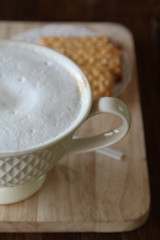Hot cappuccino and biscuit on wooden tray in morning time.