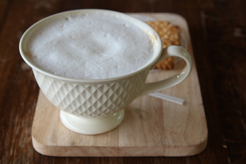 Hot cappuccino and biscuit on wooden tray in morning time.