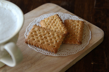 Hot cappuccino and biscuit on wooden tray in morning time.