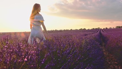 Happy Woman Enjoying Life in Lavender Field at Sunset. SLOW MOTION 120 FPS STABILIZED SHOT. Joyful girl walking in endless blooming lavender fields. Plateau du Valensole, Provence, France. Lens Flare