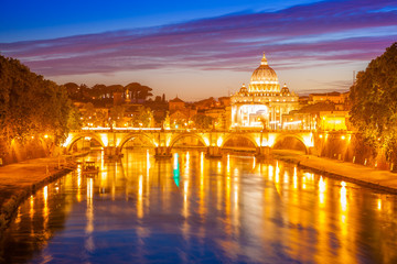 Rome skyline at night with San Pietro basilica or Saint Peter cathedral with Sant'Angelo bridge reflected on Tevere river illuminated by city lights of Roma in Italy.