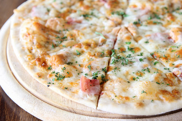 Sliced pizza with ham, sausage and vegetables on wooden tray.