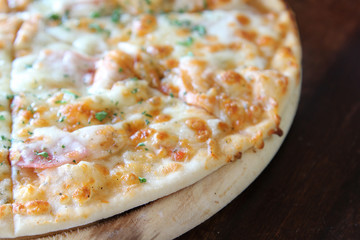 Sliced pizza with ham, sausage and vegetables on wooden tray.