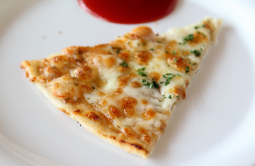 Sliced pizza with ham, sausage and vegetables on white plate.