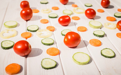 Multi-colored sliced ripe vegetables on a white wooden board background
