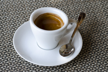 Closeup photo of coffee espresso in white porcelain cup on saucer with spoon