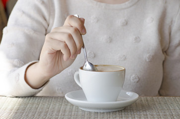 Closeup photo of a woman drinking coffee from a white porcelain cup and a saucer