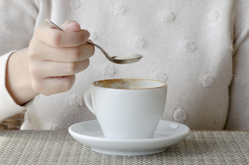 Closeup photo of a woman drinking coffee from a white porcelain cup and a saucer