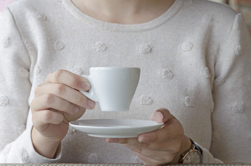 Closeup photo of a woman drinking coffee from a white porcelain cup and a saucer