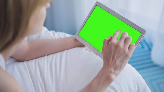 Young Woman in white top laying on bed uses Tablet PC with pre-keyed green screen. Few types of gestures - scrolling up and down, tapping, zoom in and out. Perfect for screen compositing