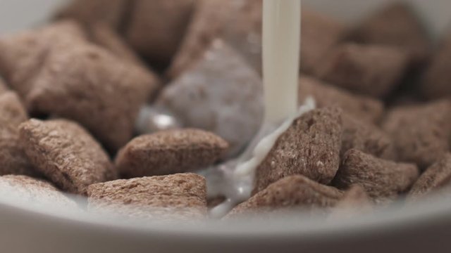 Slow motion closeup pouring milk into bowl with cereal chocolate pillows for breakfast