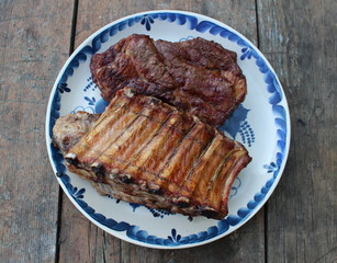 Grilled meat steaks and pork ribs on a plate on the background of an old wooden table