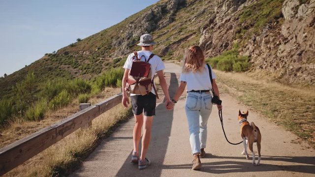 Millennials and fashion trendy woman and man walk their dog around national mountain park during sunset hours, inspirational and dreamy romantic date, loving and caring relationship
