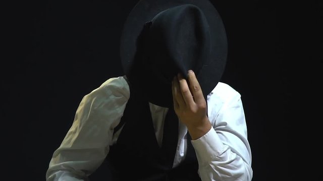 The mad detective is having fun covering his face with a black hat grimacing at the camera