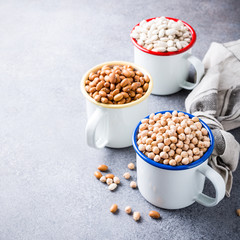 Raw uncooked organic chickpeas and kidney beans in white enamel mugs on rustic wooden board on light gray stone background. Healthy vegan vegetarian food concept with copy space.