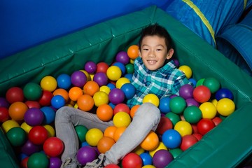 Happy boy lying in colorful balls during birthday party