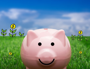 Coin bank sitting on grass with hand putting in a coin.