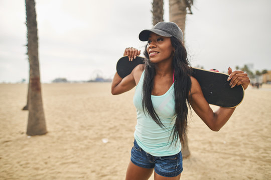 Smiling young woman holding skateboard while standing at beach