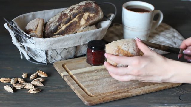 The young girl takes a roll of buckwheat bread from her basket with her young hand. Knife will cut the bun into two parts. a wooden, unprofitable village table. Coffee and a dessert with bread on a