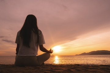 Young woman practicing yoga on the beach at sunrise.