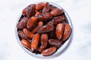 Dried dates in a silver bowl on a white marble table.